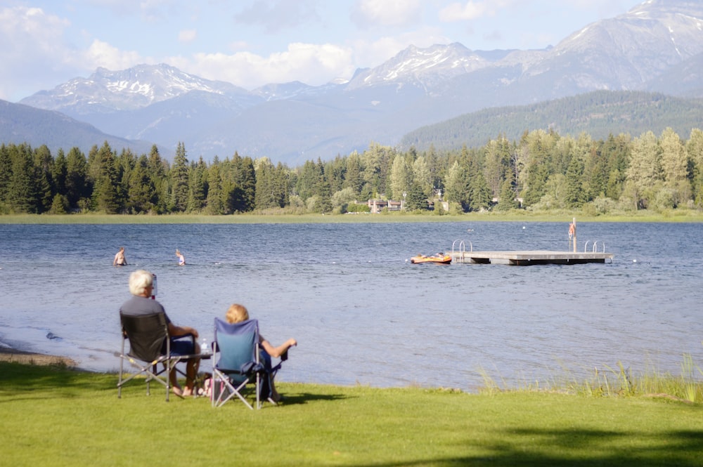 two persons sitting on grass facing the lake