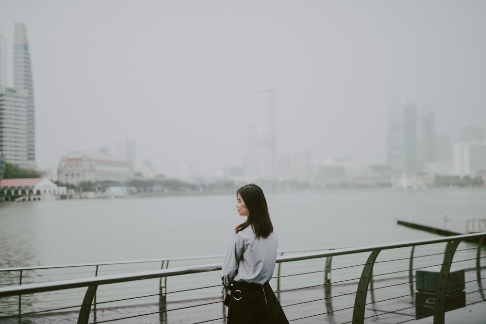 woman in gray long-sleeved shirt standing in front of body of water during daytime