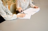 Men signing on white printer paper beside woman about to touch the documents