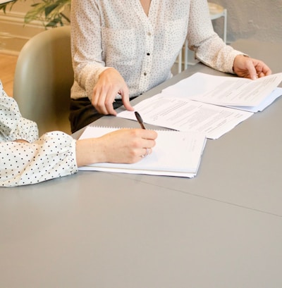 woman signing on white printer paper beside woman about to touch the documents