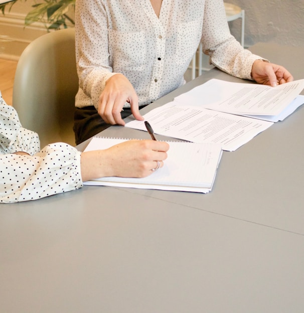 woman signing on white printer paper beside woman about to touch the documents