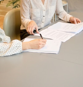 woman signing on white printer paper beside woman about to touch the documents