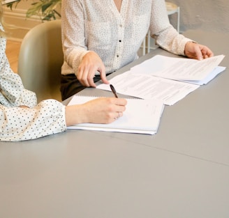 woman signing on white printer paper beside woman about to touch the documents