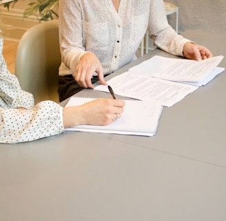 woman signing on white printer paper beside woman about to touch the documents