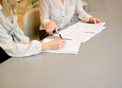 woman signing on white printer paper beside woman about to touch the documents