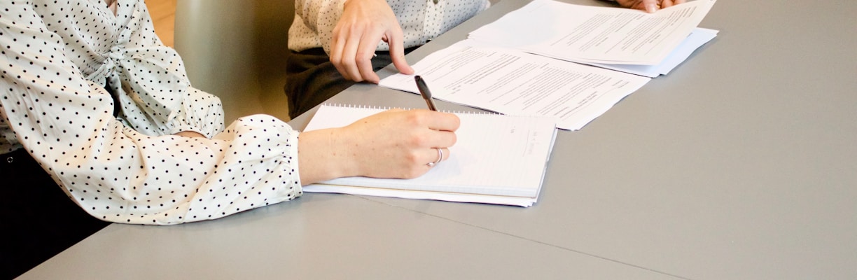 woman signing on white printer paper beside woman about to touch the documents