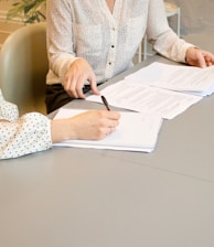 woman signing on white printer paper beside woman about to touch the documents