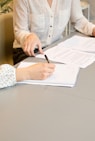 woman signing on white printer paper beside woman about to touch the documents