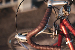 Close-up of a bike handlebar wrapped in natural leather with a backdrop of sunlit olive trees