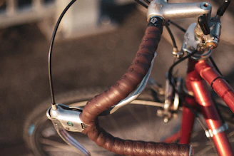 Close-up of a bike handlebar wrapped in natural leather with a backdrop of sunlit olive trees