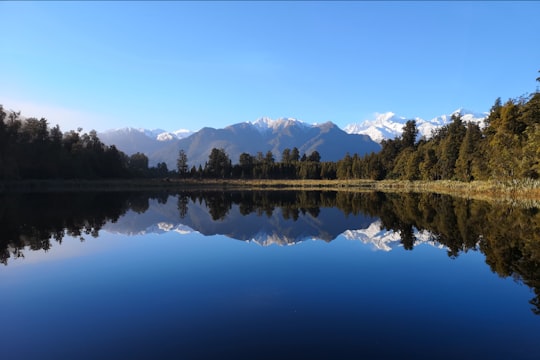 body of water surrounded by green trees during daytime in Lake Matheson New Zealand