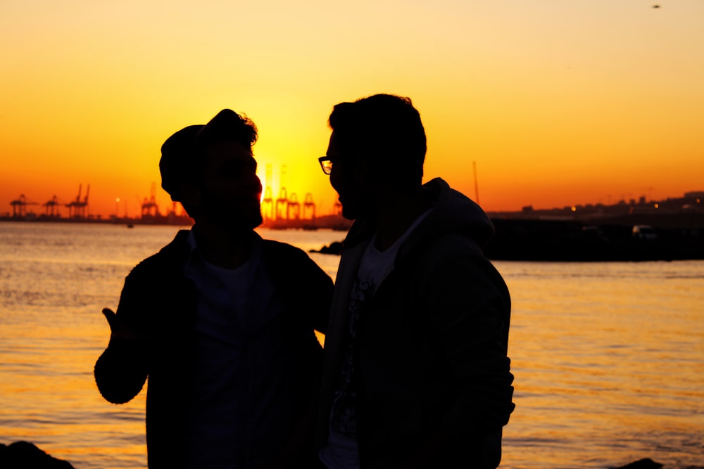 silhouette of two people standing near body of water during golden hour