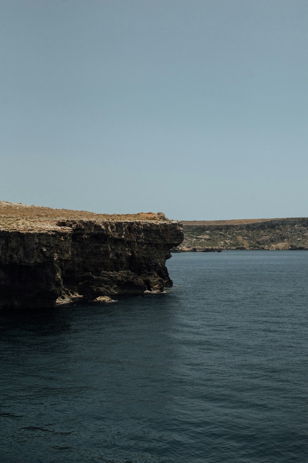 brown cliff beside body of water during daytime