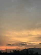 A warm, earthy-toned sunset sky over the Australian outback, with silhouetted trees and a hint of stars beginning to appear.