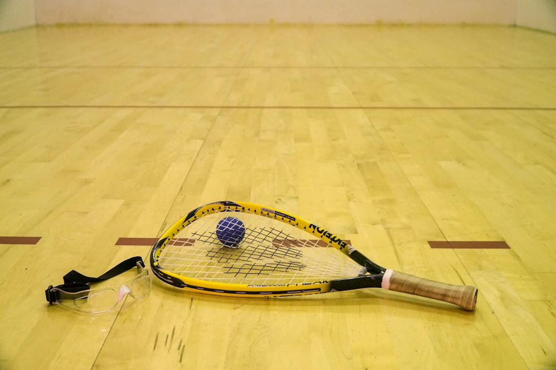 Racquetball racquet with racquetball and goggles on a wooden racquetball court inside of a recreation center