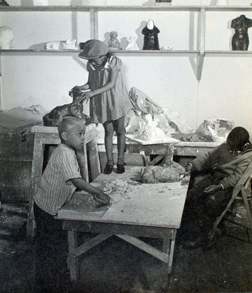 grayscale photo of 3 child on wooden table