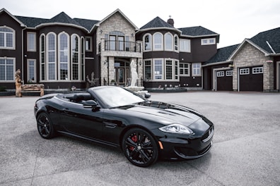 An opulent sedan parked in front of a modern mansion.