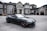 A luxurious black convertible sports car is parked in front of an opulent mansion with large windows and elaborate architectural details. The driveway is expansive, and the overall scene exudes elegance and wealth.