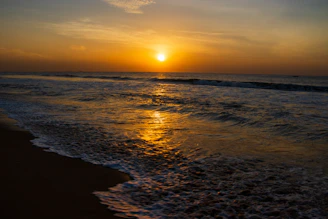 A vibrant sunset over a quiet beach, highlighting warm tones and reflections.