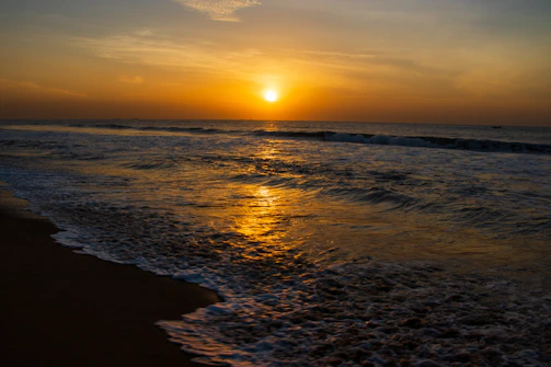 A vibrant sunset over a quiet beach, highlighting warm tones and reflections.
