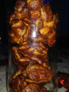 A clear glass jar filled with tightly packed dates, showcasing their rich, brown color and slightly glossy texture. The arrangement creates a dense, organic appearance, with each date's wrinkled skin and natural shape visible through the glass.