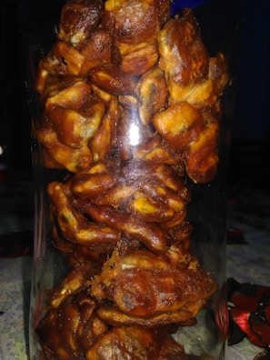A clear glass jar filled with tightly packed dates, showcasing their rich, brown color and slightly glossy texture. The arrangement creates a dense, organic appearance, with each date's wrinkled skin and natural shape visible through the glass.