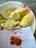 A large white plate with pink floral designs contains peeled yellow-green mango pieces and mango peels. In front of the plate, a white piece of paper is scattered with red chili flakes.
