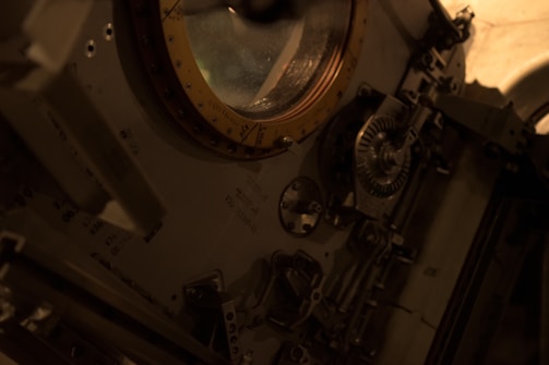 Interior view of a spacecraft module featuring a circular hatch with a golden rim. Surrounding the hatch are various mechanical components, gears, and control panels, giving it a complex and technical appearance.