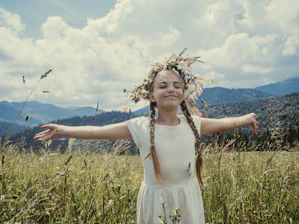 girl wearing white dress standing in the middle of grass field