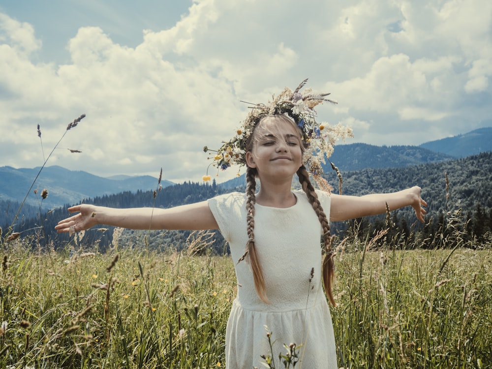 girl wearing white dress standing in the middle of grass field