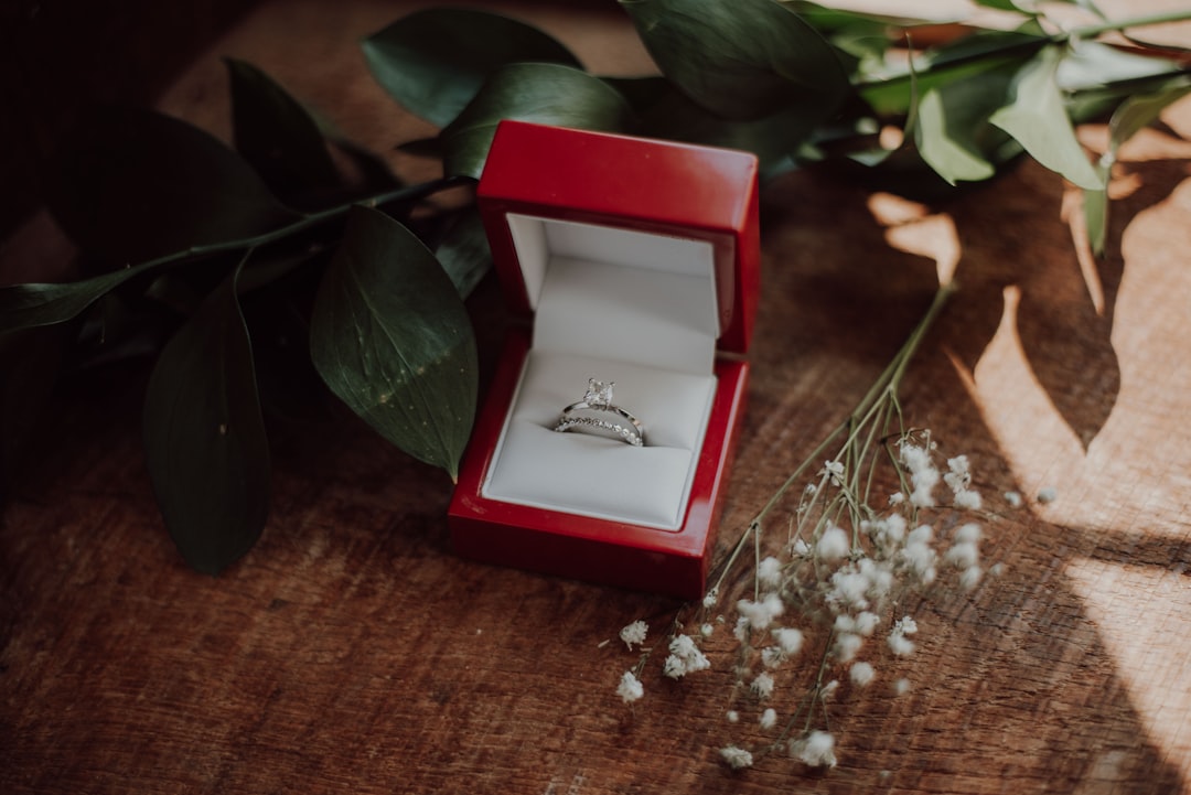 silver-colored ring in red box, A wedding band surrounded by flowers and leaves