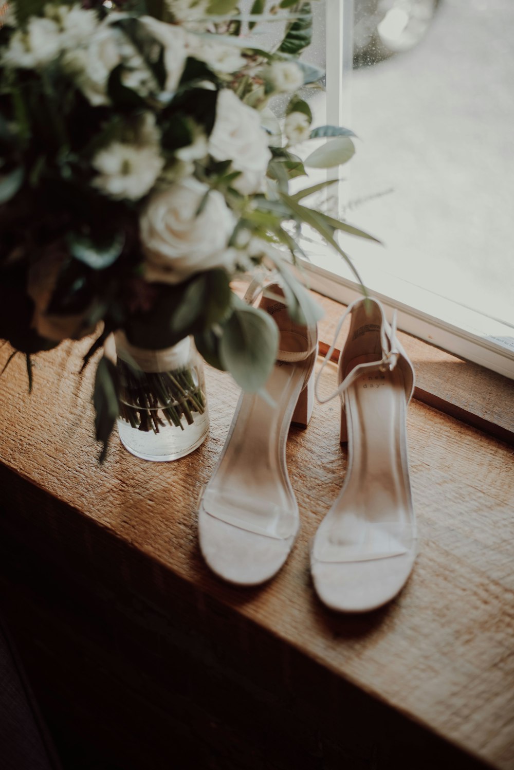 white open-toe ankle-strap heels beside flower vase