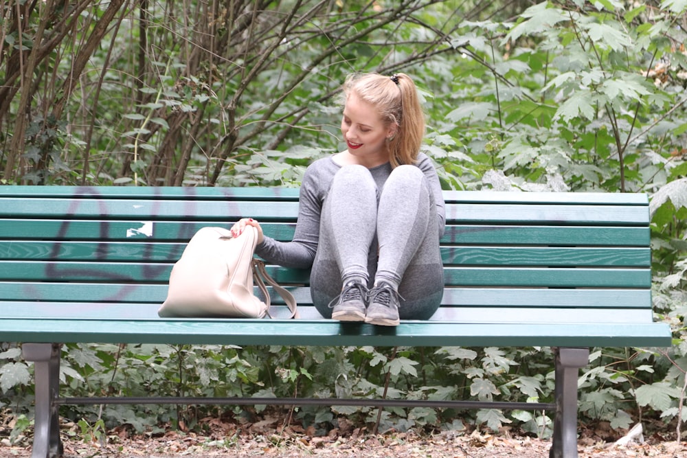 woman wearing gray long-sleeved shirt and track pants sitting on green wooden bench
