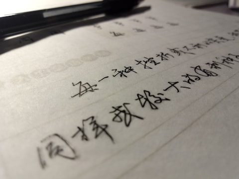 A close-up view of handwritten text in black ink on lined paper, with a pen placed at the top. The focus is on the text, while the pen and background are slightly blurred.