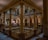An elegant interior featuring grand architectural elements such as tall, ornate columns and intricately designed railings. The lighting is warm, highlighting the detailed moldings and the stained glass window. The setting appears to be a historic or government building with a sophisticated and classic design.