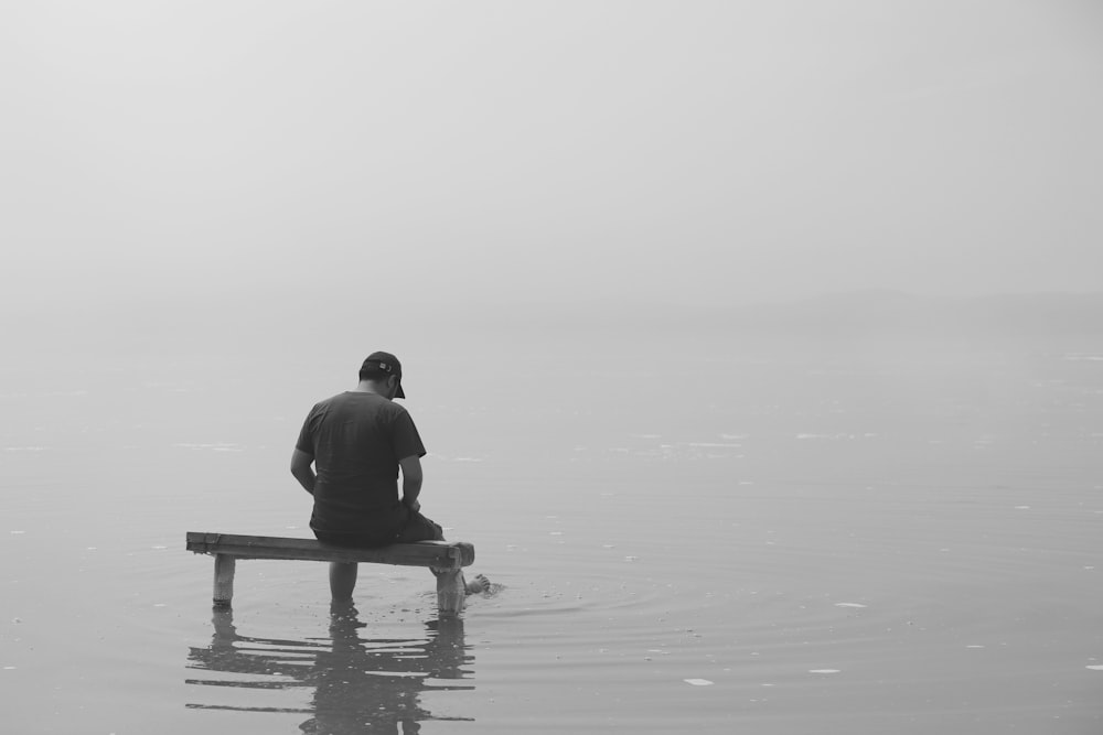 grayscale photo of man sitting on dock