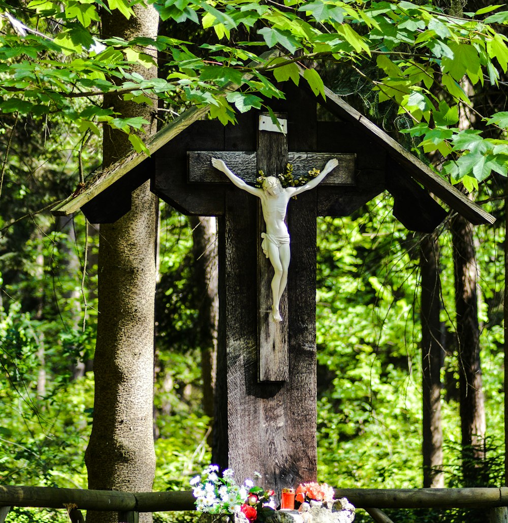 crucifix near flowers surrounded with tall and green trees