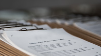 Several clipboards with stacked papers are lined up in a row on a surface. The papers appear to contain typed text and some visible headings.