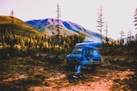 A family SUV parked beside a mountain lake with camping gear on the roof.