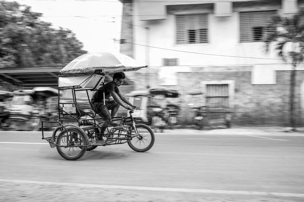 fotografia in scala di grigi persona sconosciuta che guida il triciclo