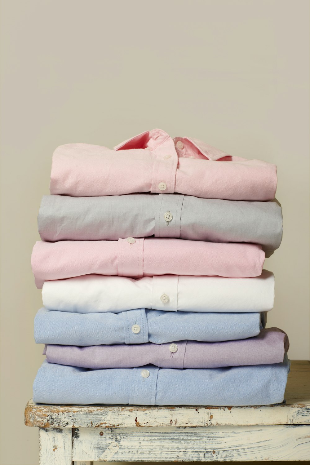 흰색 나무 테이블 위에 접힌 다양한 색상의 칼라 버튼업 셔츠