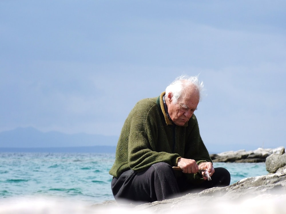 shallow focus photo of man in green long-sleeved shirt sitting near body of water