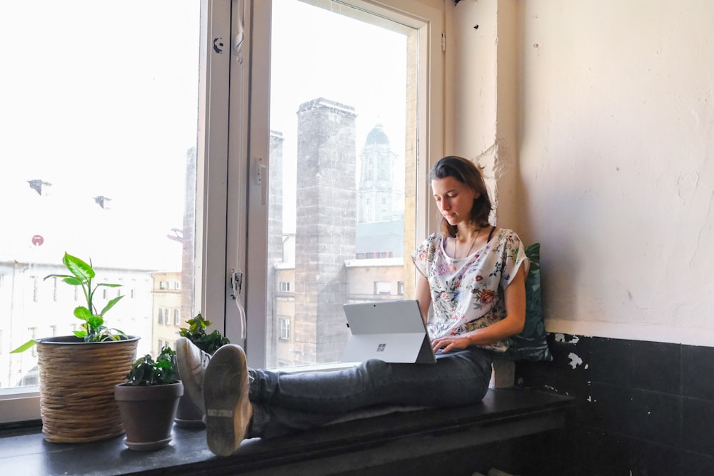 woman wearing white and red floral top sitting besides window