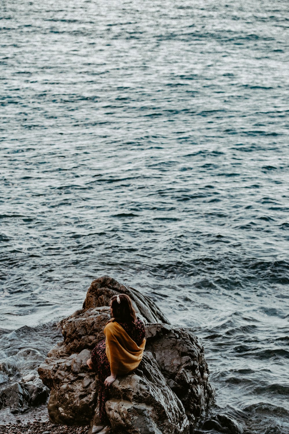 person sitting on rock beside body of water close-up photography