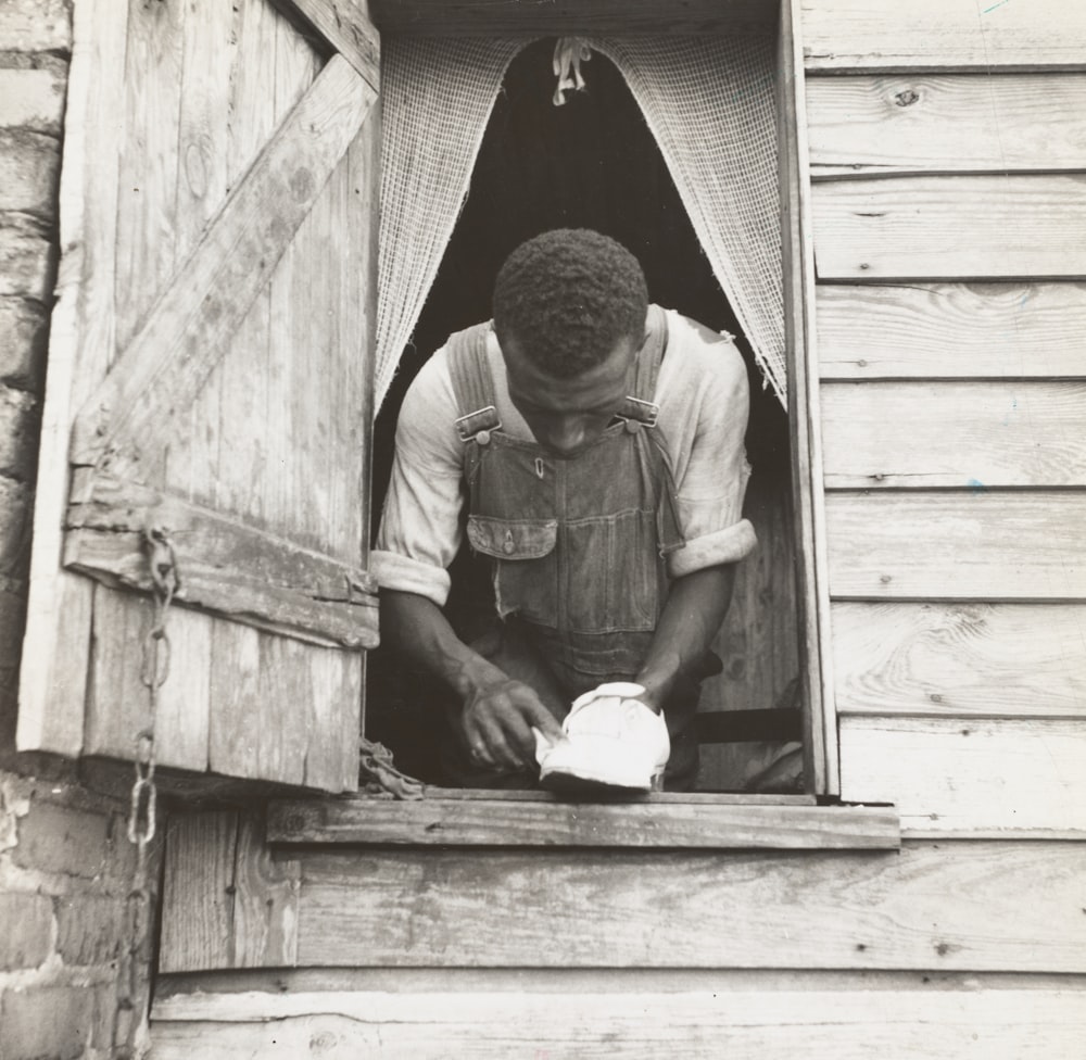 grayscale photography of man standing near open window