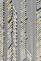 An aerial view of numerous buses parked in a large lot, arranged diagonally in rows. The buses predominantly feature white and yellow colors.