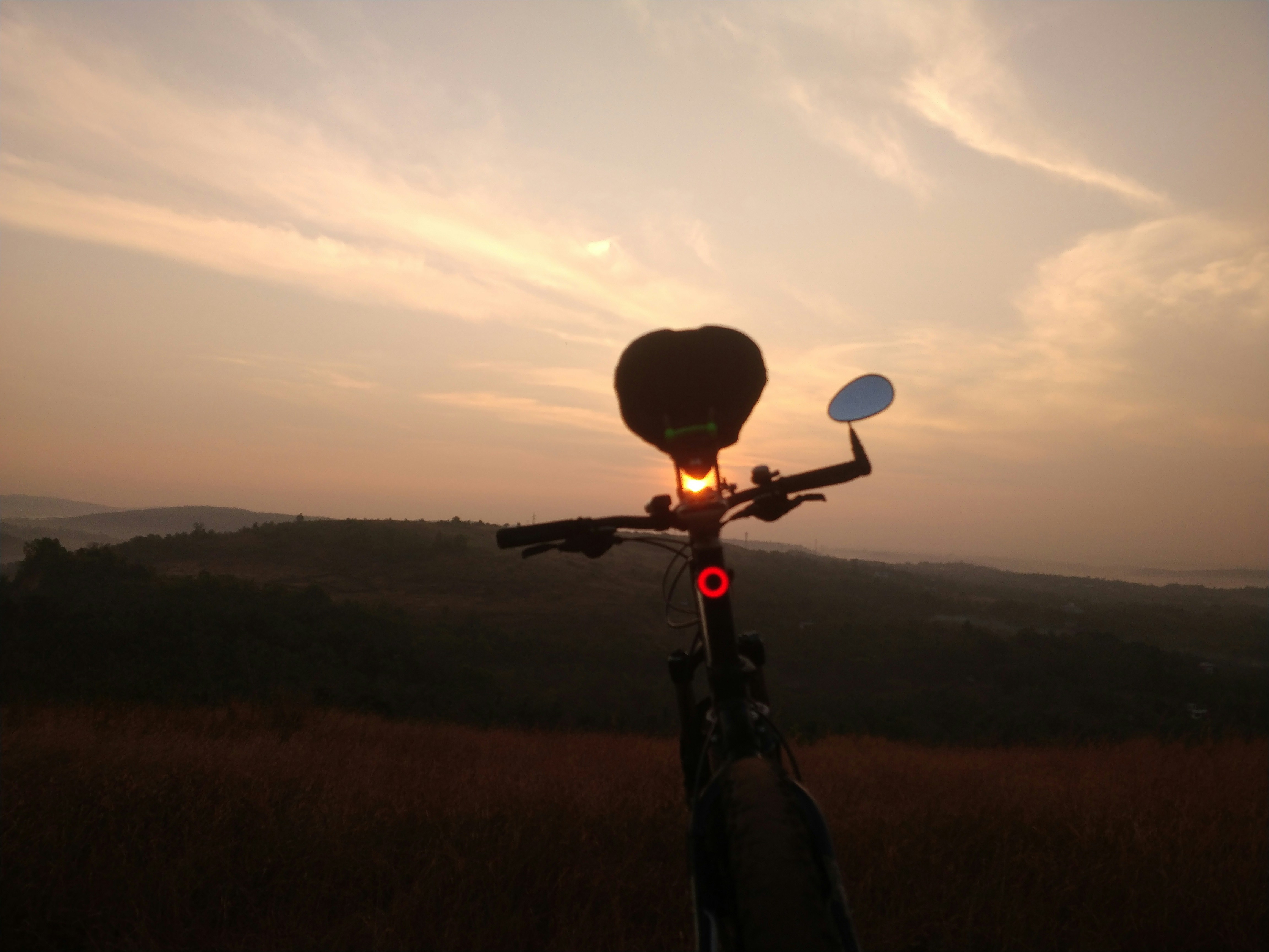 Orange sunrise over Nandi Hills with mist in the valleys, silhouette of hills, and a lone cyclist on the road