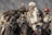 A group of people wearing traditional fur clothing is riding horses. Each person is holding a large bird, possibly an eagle, on their arm. The landscape appears rugged and mountainous, suggesting a remote location. The attire and activity suggest cultural or traditional practices related to eagle hunting.
