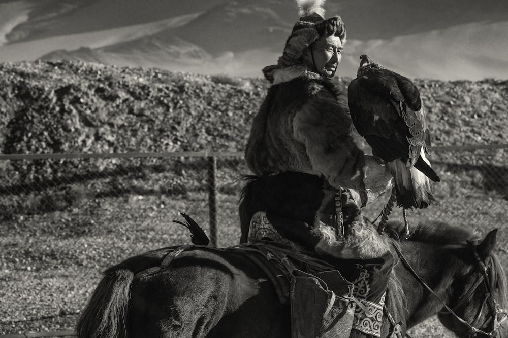 grayscale photography of man riding on horse beside eagle