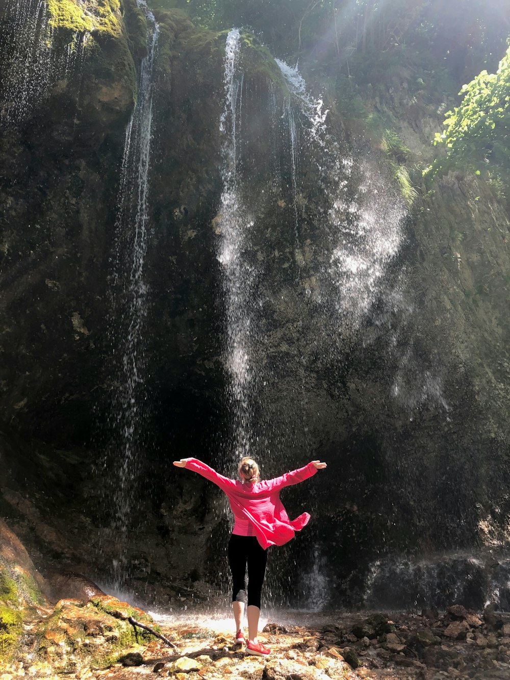 woman in red hoodie standing in front of waterfalls